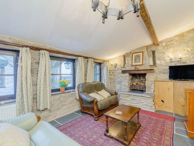 A living room with stone walls a fireplace a coffee table and seating at The Druids in Druid near Corwen