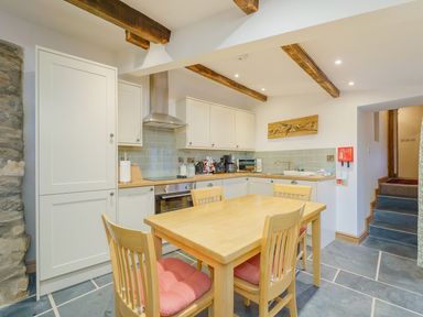 A kitchen with wooden table and chairs white cabinets and exposed wooden beams at The Druids in Druid near Corwen