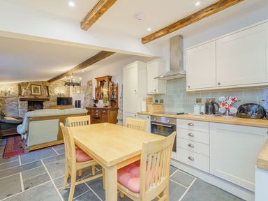 A kitchen with wooden dining table and chairs and white cabinets next to a living area with stone walls and a fireplace at The Druids in Druid near Corwen