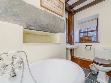 A bathroom with a bathtub toilet sink window and wooden beams at The Druids in Druid near Corwen