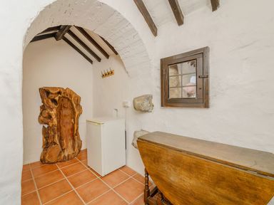 A small room with white walls and terracotta floor tiles featuring a wooden carved sculpture a small white refrigerator a wooden folding table a small window and a hook rack at The Druids in Druid near Corwen