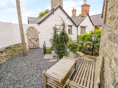An outdoor patio area with wooden bench and table near a stone wall and white building at The Druids in Druid near Corwen