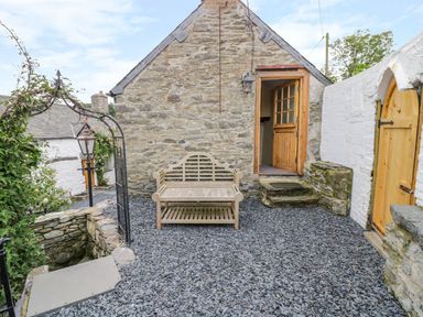A small stone courtyard with a wooden bench an open wooden door and a stone wall at The Druids in Druid near Corwen