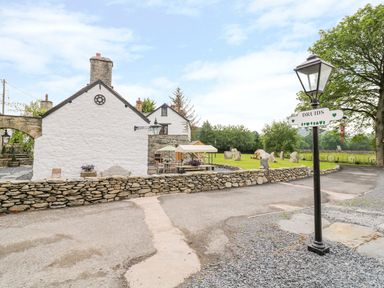 A white stone house with outdoor seating and a stone wall next to a road and green field at The Druids in Druid near Corwen