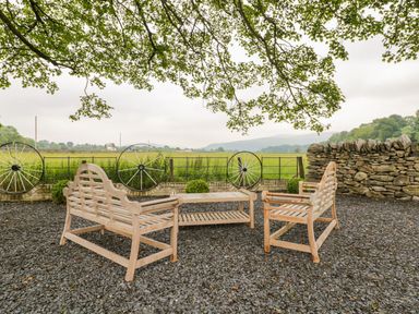 An outdoor seating area with two wooden benches a wooden table on gravel and a stone wall with a field and trees in the background at The Druids in Druid near Corwen