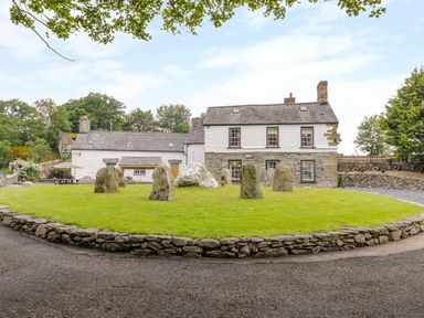 A stone circle on a grass lawn in front of a white and stone house at The Druids in Druid near Corwen