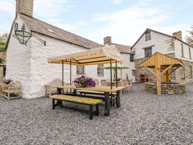 An outdoor patio area with picnic tables benches umbrellas and a stone well at The Druids in Druid near Corwen