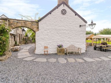 An outdoor area with stone buildings a stone arch a gravel pathway and outdoor seating at The Druids in Druid near Corwen