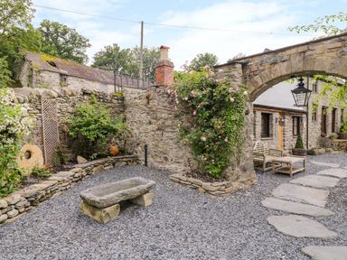 A stone courtyard with a gravel ground a stone bench climbing roses on a stone arch and outdoor seating at The Druids in Druid near Corwen
