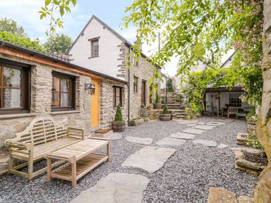 A stone courtyard with wooden bench and table outside stone cottages at The Druids in Druid near Corwen