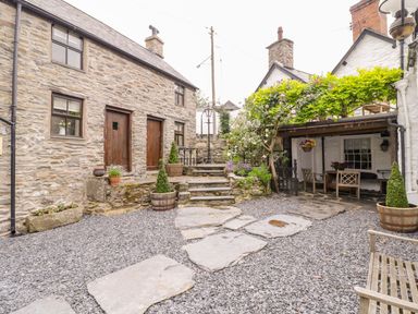An outdoor courtyard with stone steps wooden doors potted plants and a covered seating area at The Druids in Druid near Corwen