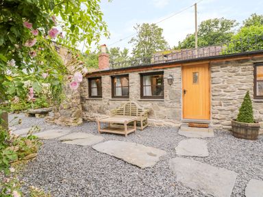 An outdoor patio area with a stone path wooden bench and table stone walls and a wooden door at The Druids in Druid near Corwen