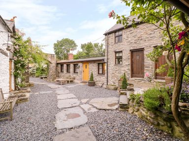 An outdoor stone courtyard with benches flowers and plants around a stone house at The Druids in Druid near Corwen