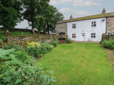 A garden with a house and stone wall at The LA'AL Cragg in Kirkby Stephen