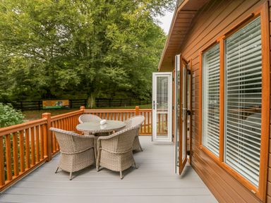 An outdoor deck with a round table and four wicker chairs next to a wooden house at Willows Lodge White Cross Bay near Windermere