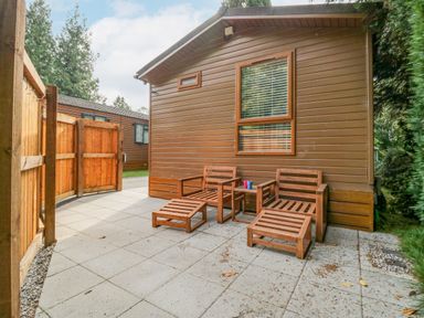 A patio area with wooden chairs and footrests outside a brown cabin at Willows Lodge in White Cross Bay near Windermere