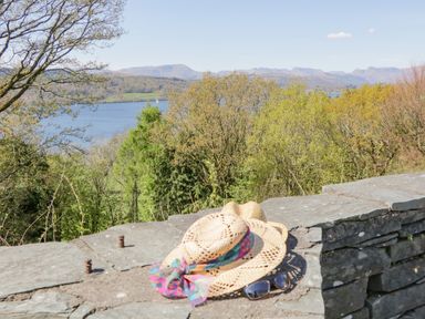 A stone wall with two straw hats and sunglasses overlooking trees and a lake at Willows Lodge in White Cross Bay near Windermere