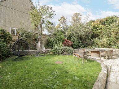 A garden with hanging chairs and a wooden table at The Old Hall in Tetbury