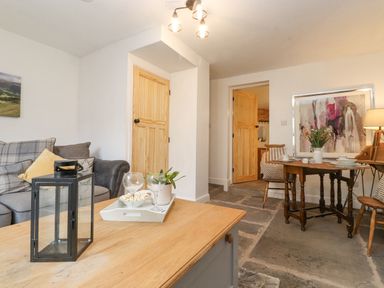 A living room with a wooden table, sofa, two doors, and dining area with chairs at The Wonky Burrow in Bowness-On-Windermere