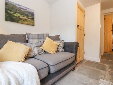 A grey sofa with yellow and plaid cushions and a white throw in a room with wooden doors and stone flooring at The Wonky Burrow in Bowness-On-Windermere