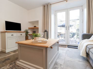 A living room with a coffee table, television on a cabinet, sofa with a blanket, and glass doors leading outside at The Wonky Burrow in Bowness-On-Windermere