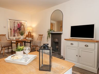 A living room with a wooden table and chairs a TV on a cabinet a fireplace and a mirror at The Wonky Burrow in Bowness-On-Windermere