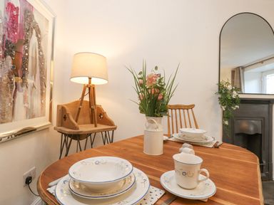 A dining area with a wooden table set with plates cups and a floral centerpiece beside a wooden chair and a standing lamp at The Wonky Burrow in Bowness-On-Windermere