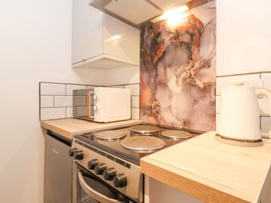A kitchen corner with an electric stove microwave kettle and wooden countertops at The Wonky Burrow in Bowness-On-Windermere