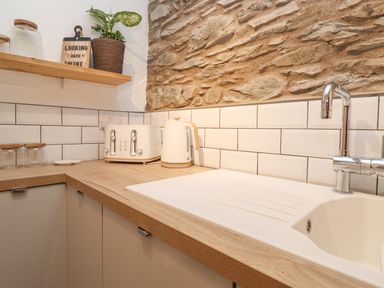 A kitchen countertop with a sink faucet toaster kettle jars plant and a sign at The Wonky Burrow in Bowness-On-Windermere