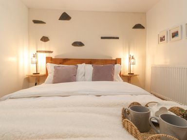 A bedroom with a wooden bed frame two bedside lamps and a tray with mugs on the bed at The Wonky Burrow in Bowness-On-Windermere