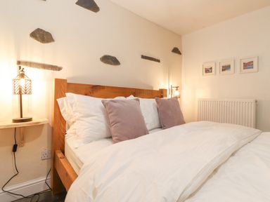 A bedroom with a wooden bed frame white bedding two bedside lamps and three framed pictures on the wall at The Wonky Burrow in Bowness-On-Windermere