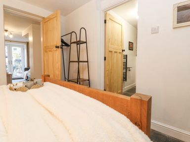 A bedroom with a wooden bed frame and white bedding a door to a bathroom an open door to a living area with glass doors at The Wonky Burrow in Bowness-On-Windermere