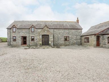 A stone house with several windows doors and a gravel driveway at Caerdegog Ganol Cemlyn near Cemaes Bay