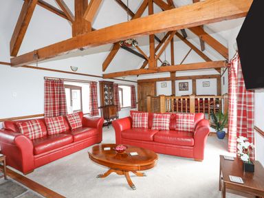 A living room with red leather sofas and wooden beams at Caerdegog Ganol in Cemlyn near Cemaes Bay