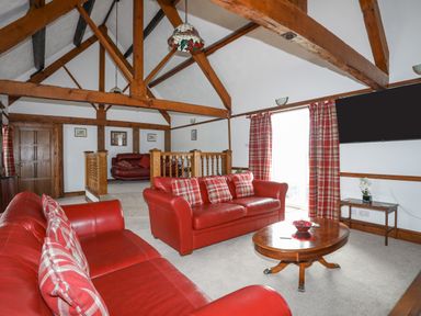 A living room with red leather sofas plaid cushions wooden beams and a round wooden coffee table at Caerdegog Ganol Cemlyn near Cemaes Bay