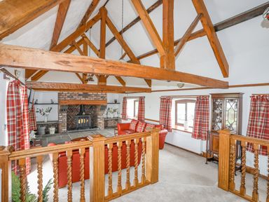 A living room with exposed wooden beams a brick fireplace and red sofas at Caerdegog Ganol in Cemlyn near Cemaes Bay