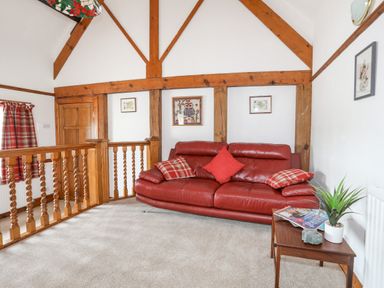A sitting area with a red leather sofa wooden beams and a side table with magazines and a plant at Caerdegog Ganol in Cemlyn near Cemaes Bay