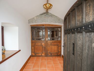 A hallway with double wooden doors with glass panels and a ceramic tile floor at Caerdegog Ganol in Cemlyn near Cemaes Bay