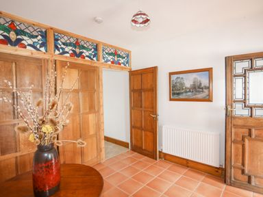 An entrance hall with wooden doors stained glass panels a radiator and a vase with dried flowers on a table at Caerdegog Ganol in Cemlyn near Cemaes Bay