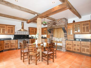 A kitchen with wooden cabinets a round dining table with six chairs and exposed wooden beams at Caerdegog Ganol in Cemlyn near Cemaes Bay