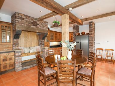 A kitchen with wooden cabinets a round dining table with chairs and a brick fireplace at Caerdegog Ganol Cemlyn near Cemaes Bay