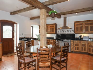 A kitchen with wooden cabinets a round dining table with six chairs and exposed wooden ceiling beams at Caerdegog Ganol in Cemlyn near Cemaes Bay