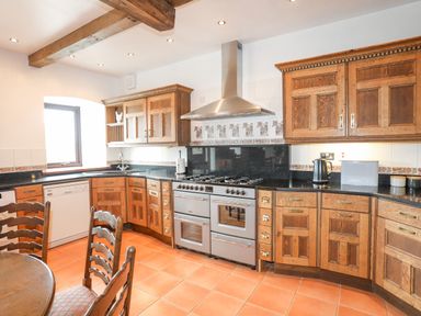 A kitchen with wooden cabinets a stainless steel stove and a round wooden table with chairs at Caerdegog Ganol in Cemlyn near Cemaes Bay