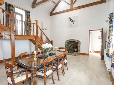 A dining room with a wooden table and chairs glass top table staircase and stone fireplace at Caerdegog Ganol Cemlyn near Cemaes Bay