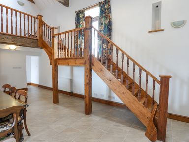 A wooden staircase with railings and floral curtains on a window near the stairs at Caerdegog Ganol in Cemlyn near Cemaes Bay