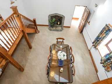 A dining area with a wooden table and six chairs near a stone fireplace and wooden staircase at Caerdegog Ganol in Cemlyn near Cemaes Bay