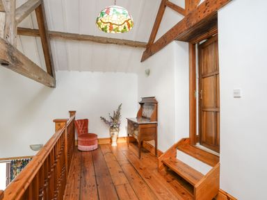 A wooden hallway with a small pink chair a vase with flowers and a wooden cabinet at Caerdegog Ganol in Cemlyn near Cemaes Bay