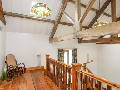 An upper floor landing with wooden railing rocking chair wooden beams and stained glass hanging lights at Caerdegog Ganol in Cemlyn near Cemaes Bay