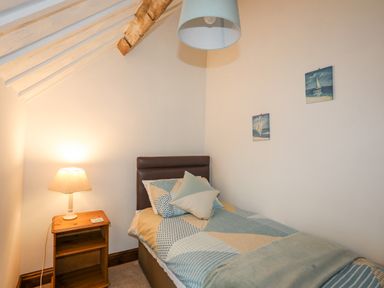 A small bedroom with a single bed a bedside table with lamp under a slanted ceiling at Caerdegog Ganol Cemlyn near Cemaes Bay