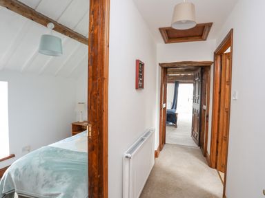 A hallway with two bedrooms visible with beds and wooden door frames at Caerdegog Ganol in Cemlyn near Cemaes Bay